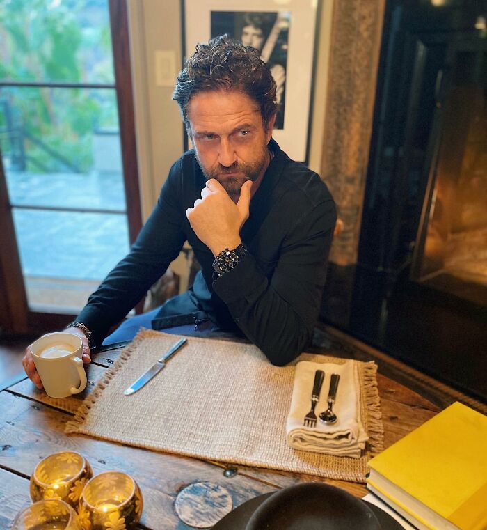 Man sitting at a wooden table holding a cup, deep in thought, unrelated to Gal Gadot skipping Venice Film Festival news.