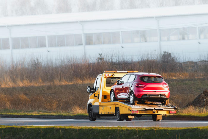 Yellow tow truck carrying red car on highway, illustrating man tows entitled neighbor&rsquo;s car after blocking his vehicle.