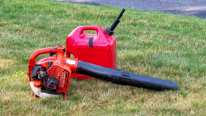 Red leaf blower and gas can on grass representing people share sounds extremely angry with outdoor noise.