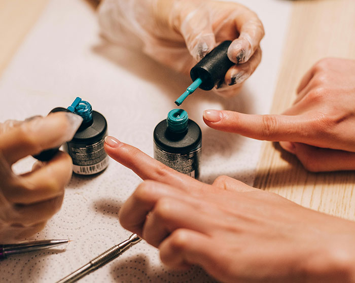 Hands applying blue gel nail polish with tools on a wooden table, illustrating gel nail polish use and application process. Hands applying blue gel nail polish with tools on a wooden table, illustrating gel nail polish use and application process.