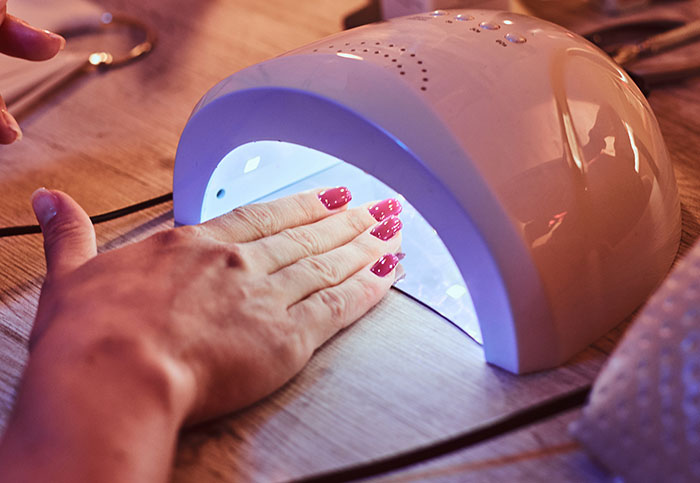 Hand with gel nail polish curing under UV lamp, illustrating why gel nail polish was banned in Europe but legal in the US Hand with gel nail polish curing under UV lamp, illustrating why gel nail polish was banned in Europe but legal in the US