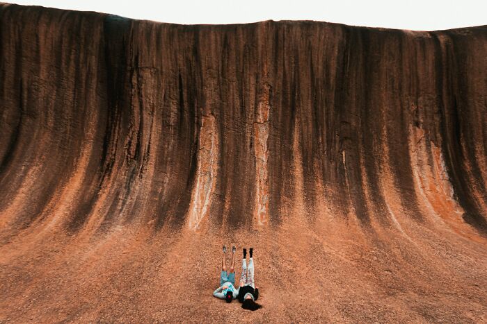 Two people lying on a curved rocky formation, showcasing unique travel destinations in person and their reality.