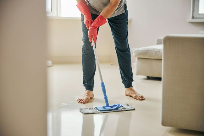 Adult wearing red gloves mopping floor barefoot in living room, illustrating adults who somehow failed to grow up.