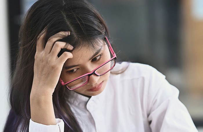 Young woman wearing pink glasses looks stressed and worried, reflecting on unexpected relationship anniversary gift.