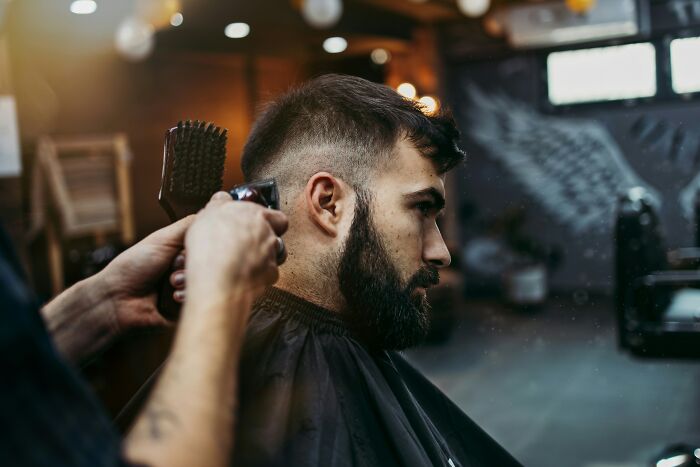 Man with a beard getting a haircut in a barbershop, illustrating suspicion when butcher and gravedigger roles combine.