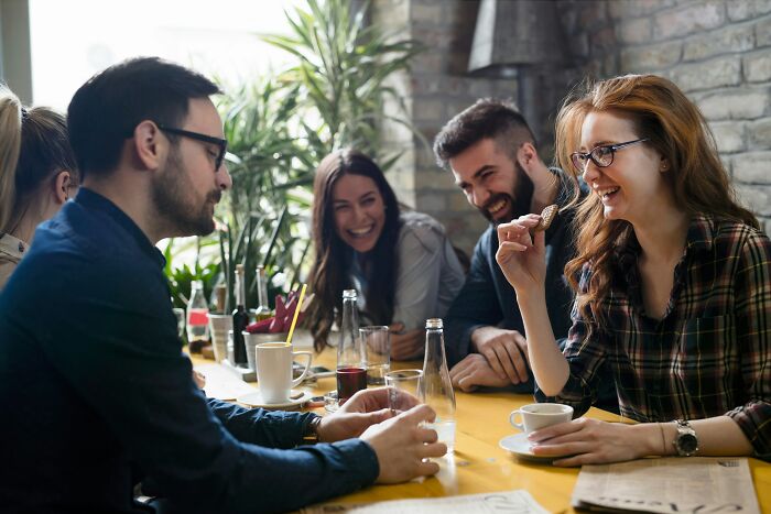 Group of people enjoying coffee and snacks at a cafe, discussing Olympic gold medalist Keely Hodgkinson and Americans being loud.
