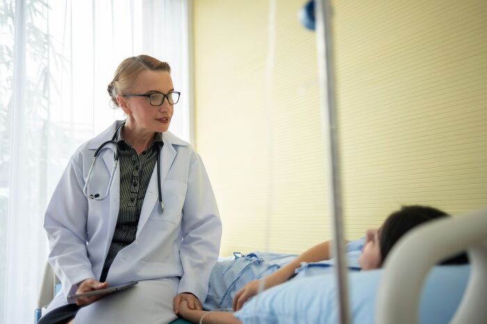 Female doctor consulting a teenage girl in hospital bed, highlighting risks of meningitis misdiagnosis in young patients.