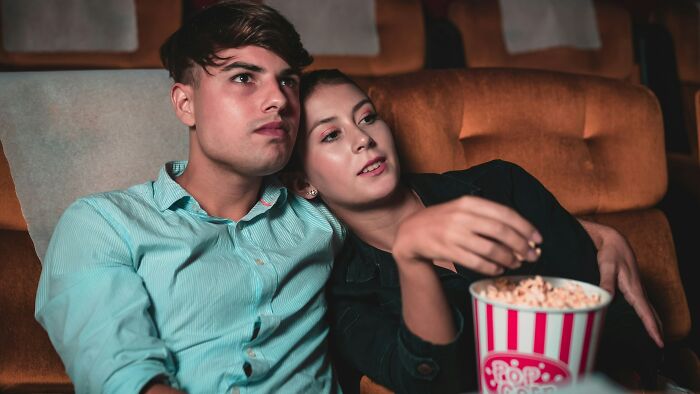 A young couple sitting close in a theater, sharing popcorn while watching a movie, illustrating relationship dealbreakers.