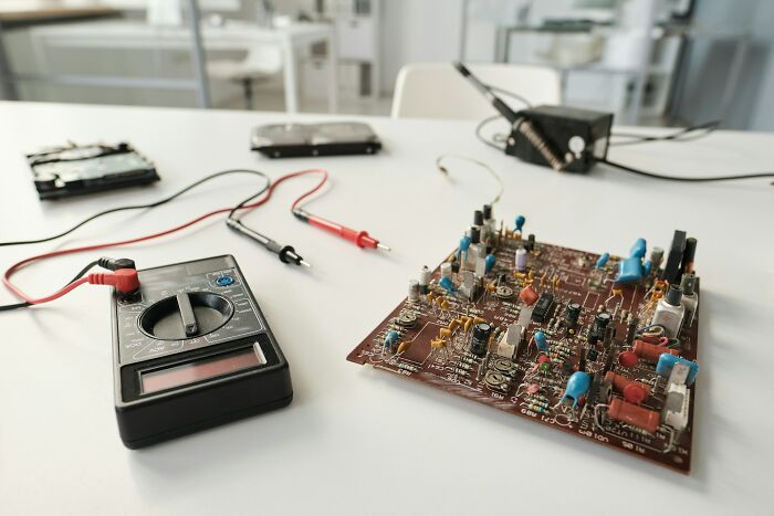 Multimeter and electronic circuit board on a white table, tools used for testing before fast firing decision.