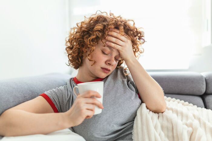 Young woman with curly hair holding a mug and looking distressed, reflecting on experiences with school bullies.