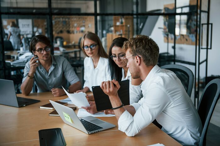 Four young professionals in a modern office engaged in a discussion about advanced stupid ideas and out-of-touch concepts.