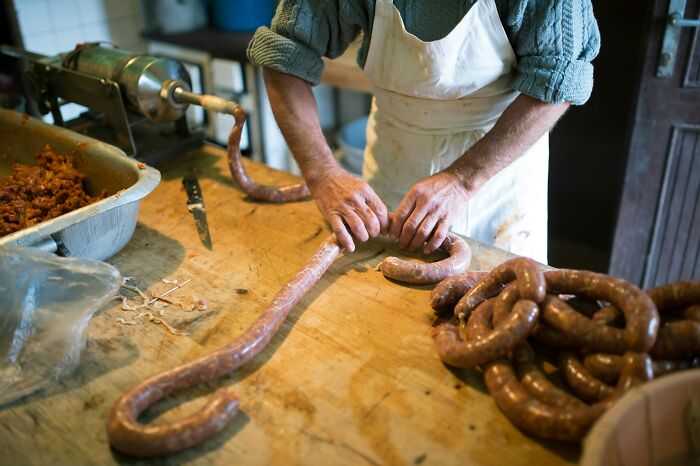 Person in an apron making sausages by hand at a wooden table, illustrating butcher-related profession tasks.