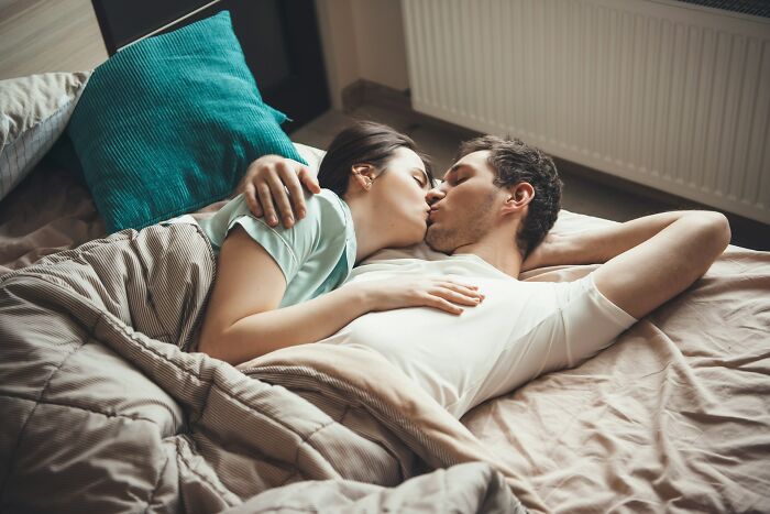 Couple lying in bed kissing, capturing moments from dating experiences that show signs of dating an idiot.