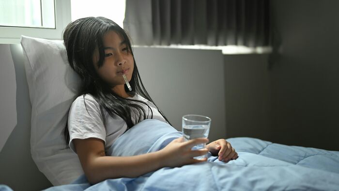 Young girl in bed with a thermometer and glass of water, showing the impact of bold decisions on health worldwide.