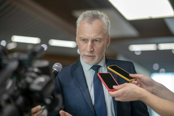 Man in a suit speaking to reporters, illustrating the impact of school bullies and revealing their life outcomes.