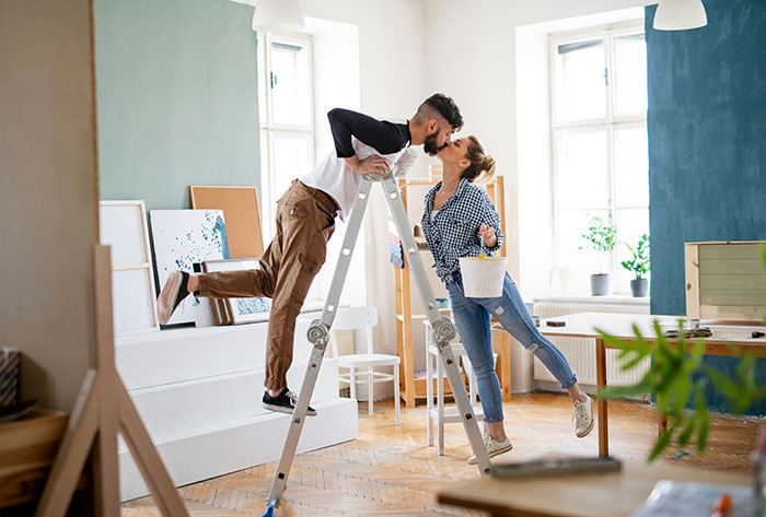 Couple sharing a kiss while painting their home, hinting at a guy convinced he took an art class with his girlfriend.