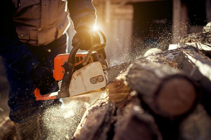 Person using a chainsaw to cut wood outdoors with sunlight and dust particles in the air, medical odd patients theme.