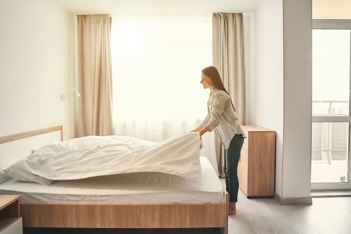 Woman making a bed in a bright room, illustrating jobs that exist solely for ultra-wealthy people according to netizens.