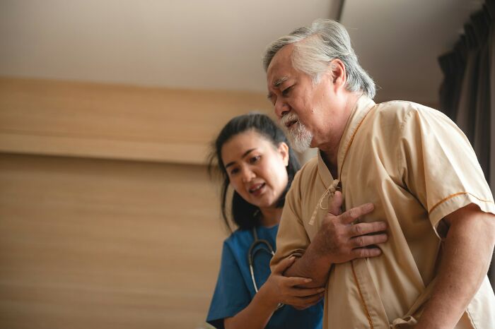 Older male patient clutching chest assisted by nurse, illustrating patients who defied medical odds with doctor support.