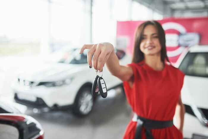Woman in red dress holding car keys inside dealership, illustrating Americans finding a loophole and using it creatively.