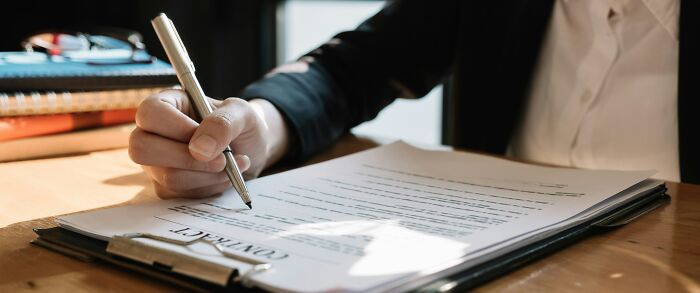 Person writing and signing a contract on a clipboard at a wooden desk highlighting companies that sabotage their own products.