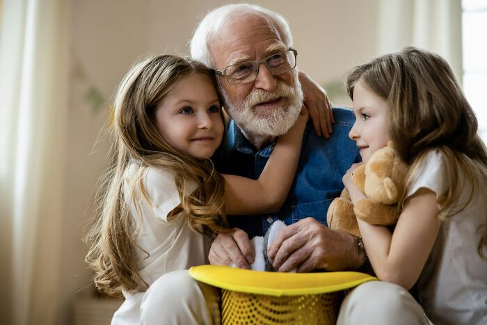 Elderly man with glasses hugging two young girls, illustrating emotional family secrets revealed and shared moments.