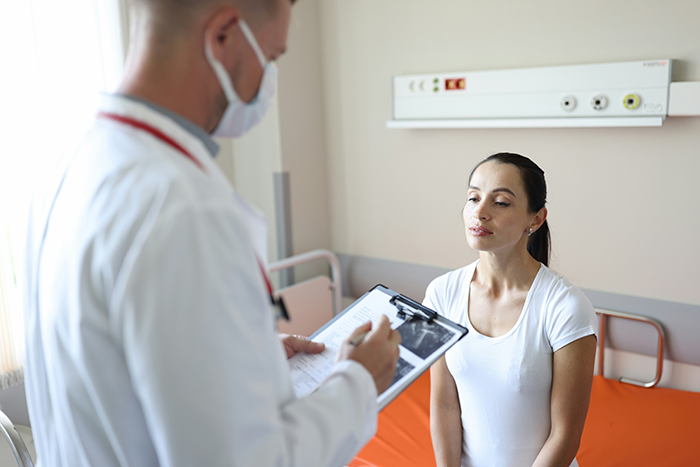 Doctor in a medical mask reviews patient notes with a woman in a white shirt during a consultation about infections.