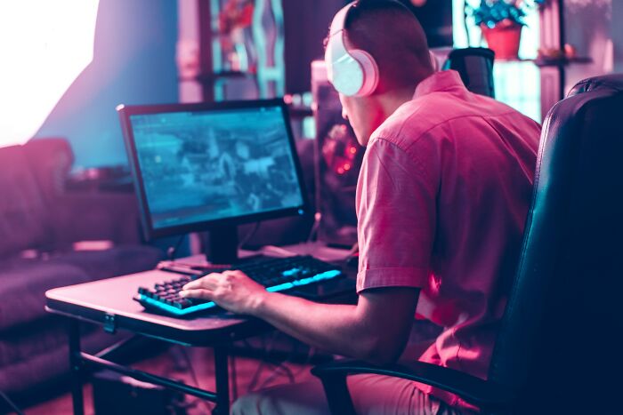 Adult wearing headphones playing video games on computer, illustrating adults who failed to understand growing up is mandatory.
