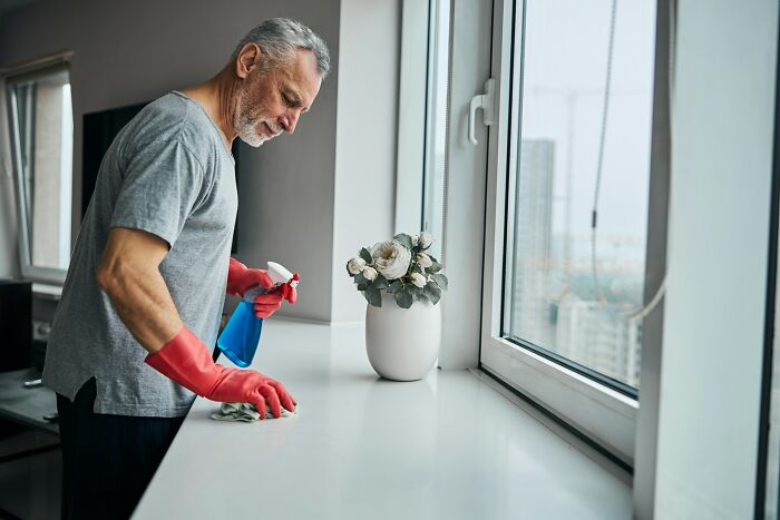 Older man cleaning windows in a bright room, symbolizing men in happy marriages keeping a great relationship.