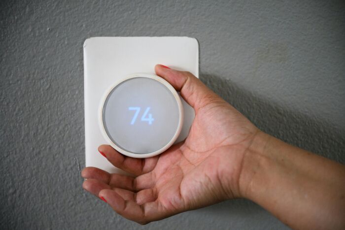 Hand adjusting a digital thermostat showing 74 degrees, illustrating companies that sabotage their own products examples.