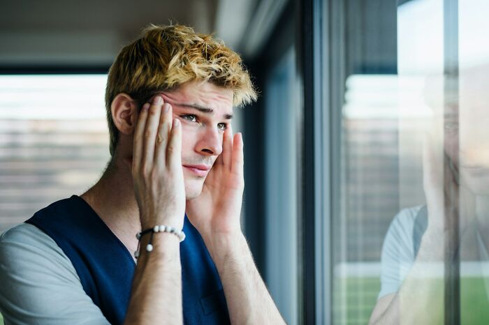 A young man looking stressed and worried while staring out a window, reflecting on fast ways people get fired.