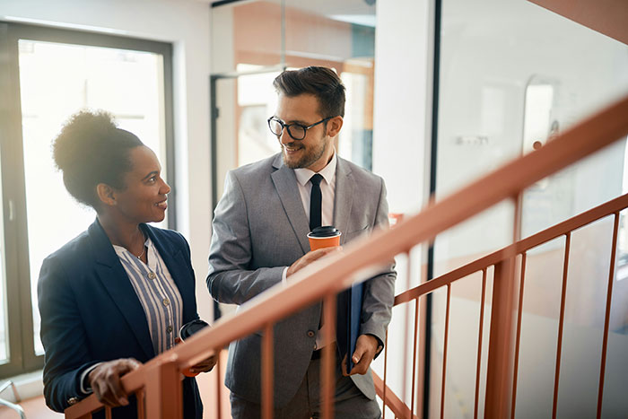 Two coworkers in business attire having a casual conversation indoors, illustrating creepy coworker petty response concept.