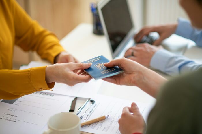 Two people exchanging a passport over a desk with documents and a laptop, highlighting dating idiot moments.