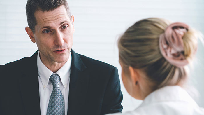 Man in suit speaking seriously to coworker with hair in bun, illustrating creepy coworker petty response in office setting.