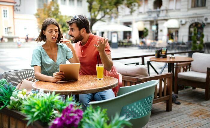 Couple having a tense argument at an outdoor café, illustrating exact moments people knew they were dating an idiot.