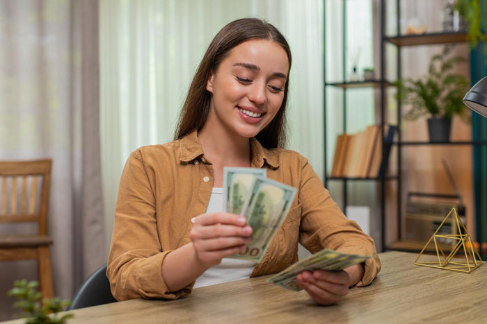 Young woman smiling counting money at home, representing girlfriend wants to quit job after winning lottery with excitement.