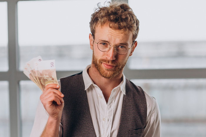 Man with glasses holding cash, symbolizing lottery winnings, reflecting a girlfriend wanting to quit job decision.