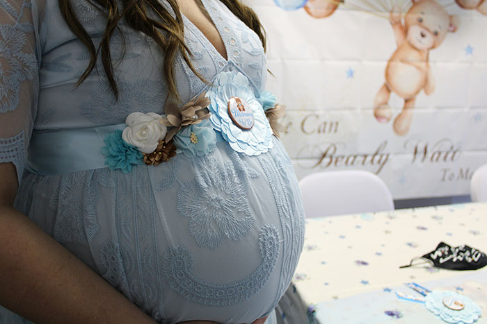 Pregnant woman wearing a blue dress at a baby shower, highlighting strong opinions on grandmas having a baby shower.