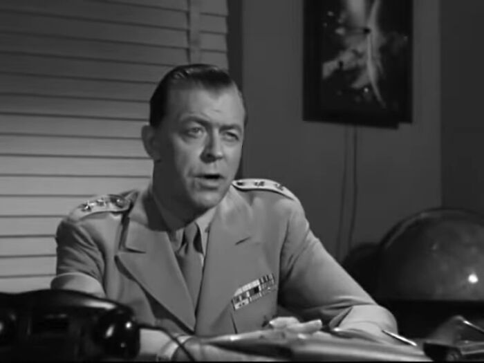 Black and white scene from a classic worst-best movie showing a man in a military uniform at an office desk.