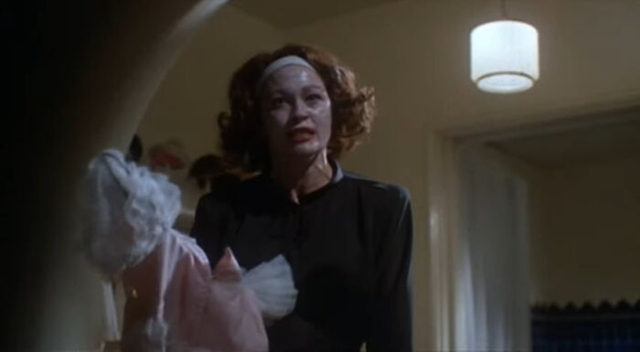 Scene from a worst-best movie showing a woman with messy hair holding a doll in a dimly lit room.