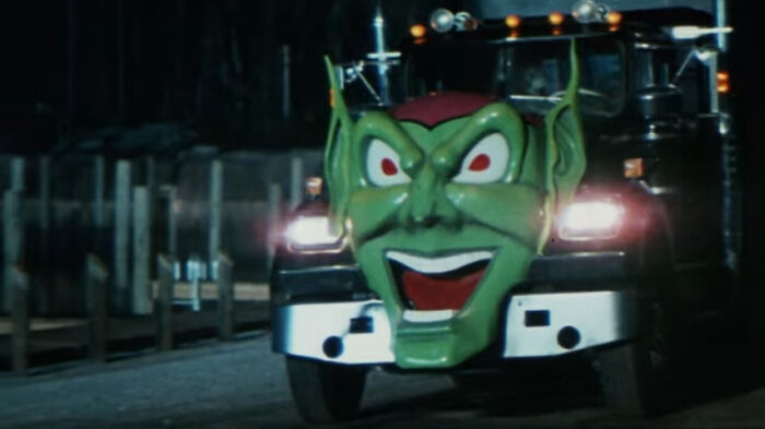 A truck with a large green goblin face on the front driving at night, featured in worst-best movies people enjoy.