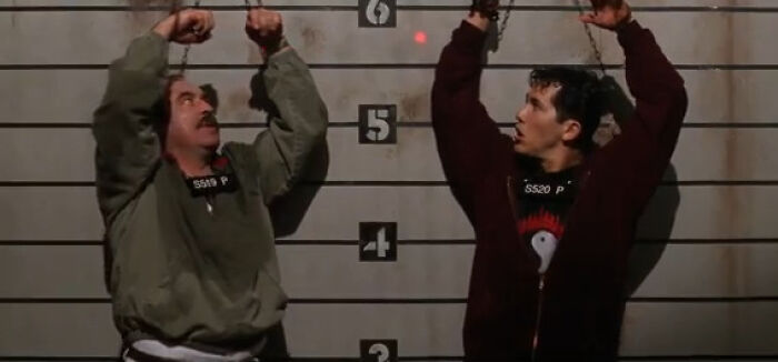 Two men handcuffed and chained against a height chart, illustrating worst-best movies that people actually enjoy.