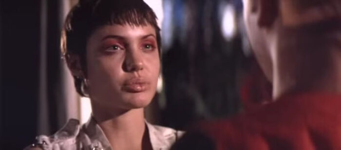 Close-up of a woman with short hair and bruised eyes facing a man in a dimly lit scene from worst-best movies.