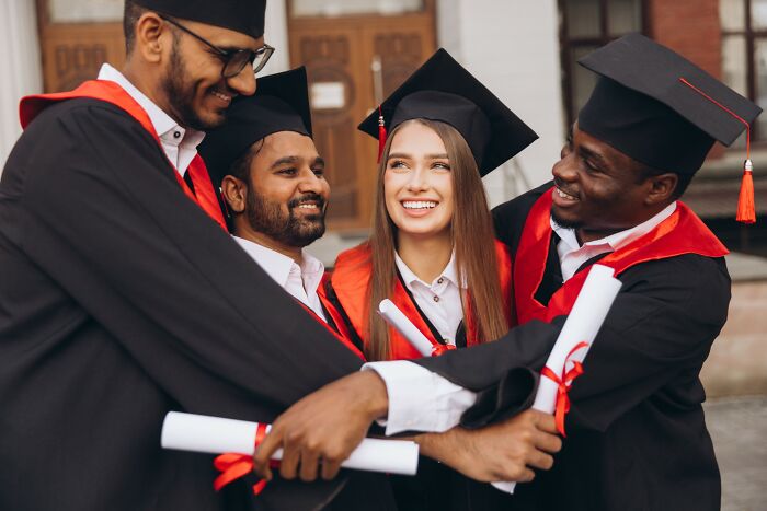 Group of diverse graduates in caps and gowns happily holding diplomas, celebrating a loophole moment together outdoors