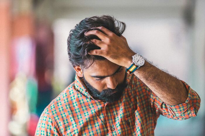 Man in a checkered shirt looks stressed, holding his head, illustrating the fastest ways people get fired.