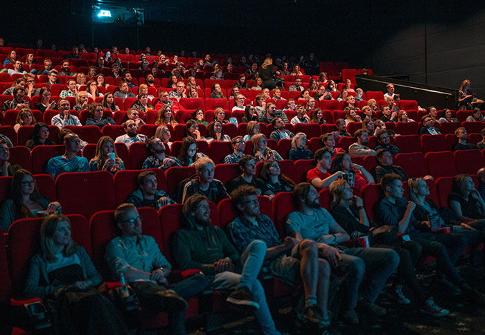 Audience seated in a dark theater, attentively watching a movie about people thankful for listening to their instincts.