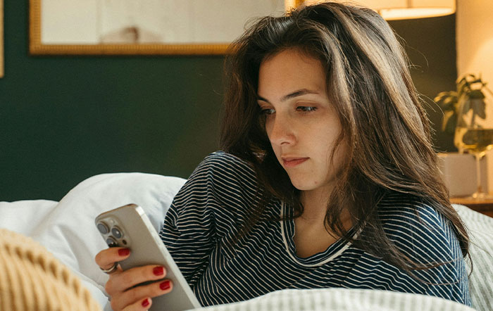 Woman with long hair reading phone in bed, reflecting on moments when people trusted their instincts and felt thankful.