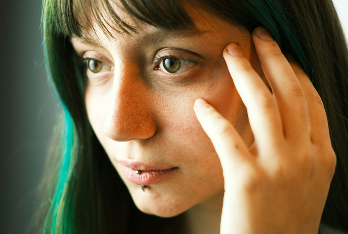 Young woman with green hair touching her face, deep in thought, illustrating trusting instincts in a tense moment.