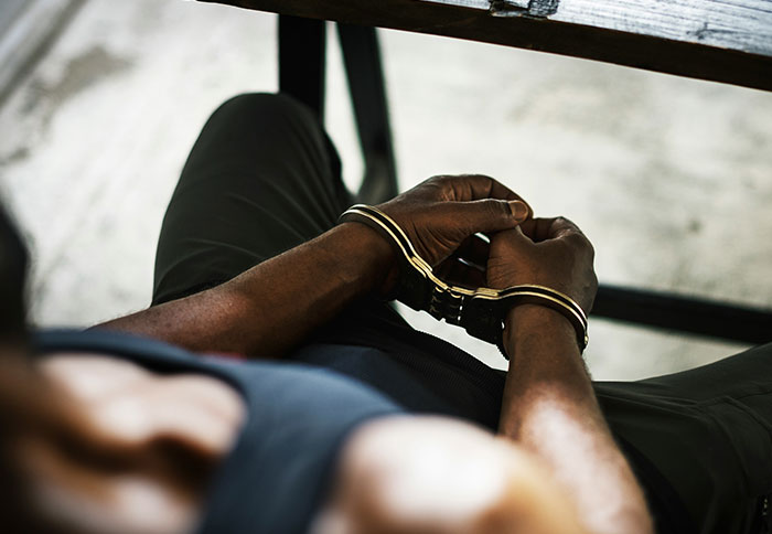 Close-up of a person in handcuffs sitting on a bench, highlighting the importance of trusting instincts in dangerous situations.