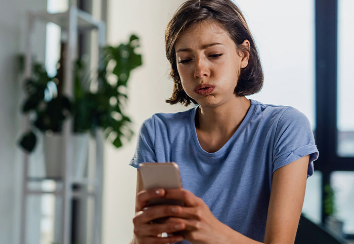 Young woman in a blue shirt looking concerned while checking her phone, illustrating listening to instincts and being thankful.